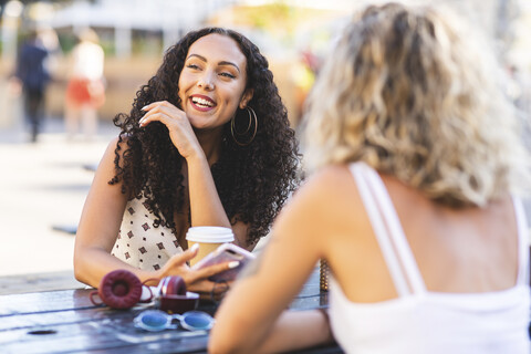 Zwei glückliche Freunde unterhalten sich am Tisch im Freien, lizenzfreies Stockfoto