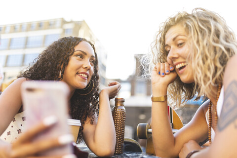 Zwei glückliche Freunde teilen sich ein Mobiltelefon im Freien, lizenzfreies Stockfoto