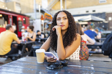 Beautiful young woman with cell phone sitting at a table and waiting - WPEF00797