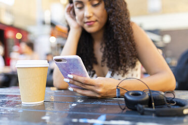 Junge Frau sitzt an einem Tisch und schaut auf ihr Handy - WPEF00798