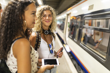 UK, London, zwei junge Frauen mit Handys warten am Bahnsteig einer U-Bahn-Station - WPEF00800