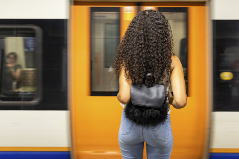 Großbritannien, London, Rückansicht einer jungen Frau, die am Bahnsteig einer U-Bahn-Station wartet, lizenzfreies Stockfoto