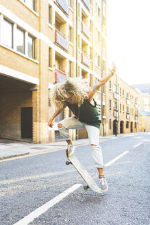 Junge Frau macht Tricks mit ihrem Skateboard in der Stadt - WPEF00804