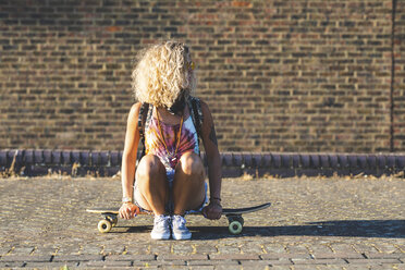 Junge Frau, die auf einem Skateboard sitzt, mit einer Backsteinmauer im Hintergrund - WPEF00810