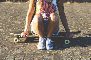 Close-up of young woman sitting on a skateboard in sunlight - WPEF00812