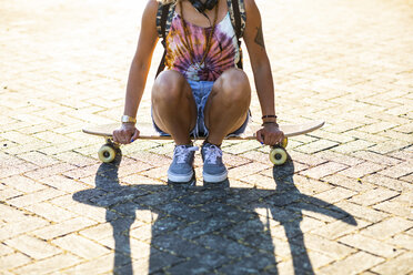 Close-up of young woman sitting on a skateboard in sunlight - WPEF00813