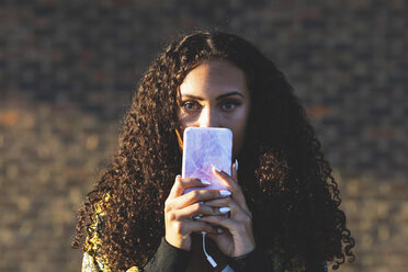 Portrait of young woman with curly hair holding cell phone - WPEF00815