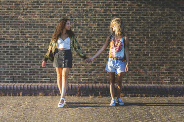 Two young women holding hands in front of brick wall - WPEF00822