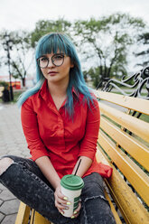 Porträt einer jungen Frau mit gefärbten blauen Haaren, die auf einer Bank mit einem Getränk sitzt - VPIF00825