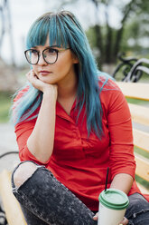 Porträt einer jungen Frau mit gefärbten blauen Haaren, die auf einer Bank mit einem Getränk sitzt - VPIF00826