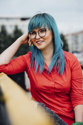 Porträt einer lächelnden jungen Frau mit gefärbten blauen Haaren, die auf einer Bank mit einem Getränk sitzt - VPIF00828