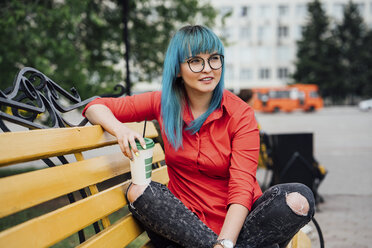 Porträt einer jungen Frau mit gefärbten blauen Haaren, die auf einer Bank mit einem Getränk sitzt - VPIF00829
