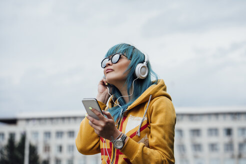 Porträt einer jungen Frau mit gefärbten blauen Haaren, die mit Smartphone und Kopfhörern Musik hört - VPIF00838