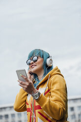 Porträt einer jungen Frau mit gefärbten blauen Haaren, die mit Smartphone und Kopfhörern Musik hört - VPIF00839