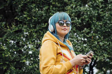 Porträt einer jungen Frau mit gefärbten blauen Haaren, die mit Smartphone und Kopfhörern Musik hört - VPIF00841