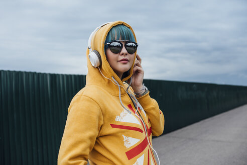 Porträt einer jungen Frau mit gefärbten blauen Haaren, die mit Kopfhörern Musik hört - VPIF00845