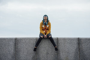 Junge Frau mit gefärbten blauen Haaren, die auf einer Mauer sitzt und nach oben schaut - VPIF00862