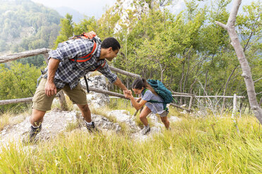 Italy, Massa, man helping a young woman to climb a step while hiking in the Alpi Apuane mountains - WPEF00851