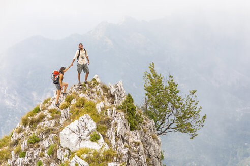 Italy, Massa, man helping woman to climb on top of a peak in the Alpi Apuane mountains - WPEF00858