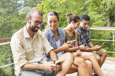 Italy, Massa, hikers in the Alpi Apuane mountains looking at their smartphones and sitting on a bench - WPEF00885