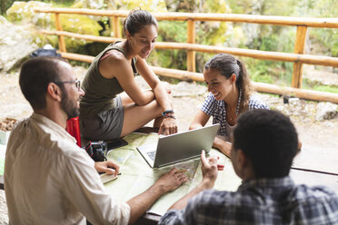 Eine Gruppe von Wanderern sitzt zusammen und plant eine Wanderroute mit Karte und Laptop - WPEF00905