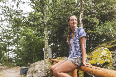 Italy, Massa, smiling young woman sitting on a wooden fence in the Alpi Apuane - WPEF00910