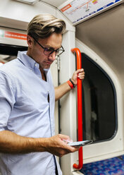 UK, London, Geschäftsmann in U-Bahn-Zug schaut auf Handy - MGOF03793