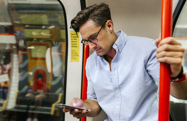 UK, London, Geschäftsmann in U-Bahn-Zug schaut auf Handy - MGOF03795