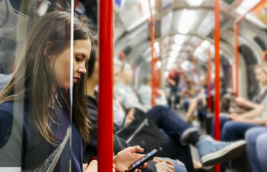 UK, London, young woman in underground train looking at cell phone - MGOF03796