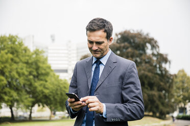 Geschäftsmann benutzt Mobiltelefon im Stadtpark - MOEF01382