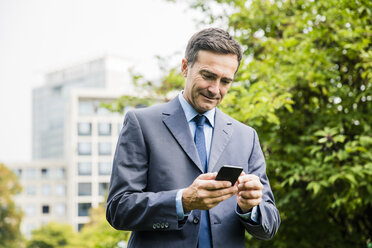 Businessman using cell phone in city park - MOEF01384