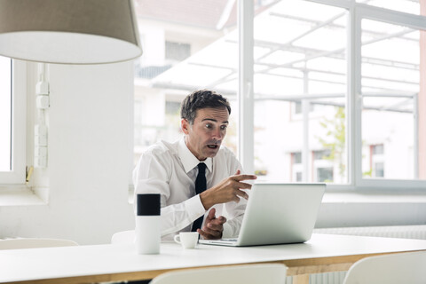 Geschockter Geschäftsmann schaut auf den Laptop auf dem Tisch im Büro, lizenzfreies Stockfoto