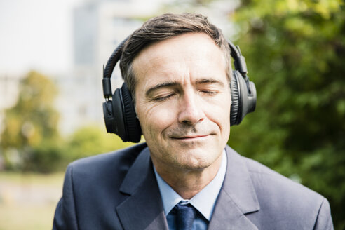 Businessman with closed eyes listening to music with headphones - MOEF01393