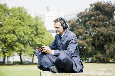 Geschäftsmann im Stadtpark, der Kopfhörer trägt und ein Tablet benutzt - MOEF01395