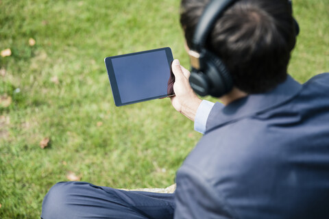 Geschäftsmann trägt Kopfhörer und benutzt ein Tablet im Freien, lizenzfreies Stockfoto