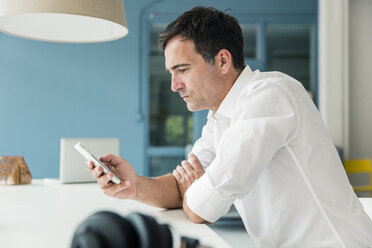 Seriöser Geschäftsmann schaut auf sein Handy im Büro - MOEF01400