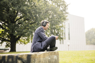 Businessman in city park wearing headphones and using tablet - MOEF01401