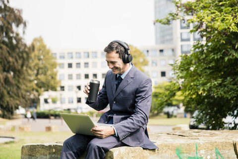 Geschäftsmann im Stadtpark, der Kopfhörer trägt und einen Laptop benutzt, lizenzfreies Stockfoto