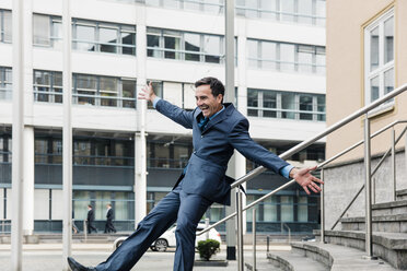 Carefree businessman sliding down railing in the city - MOEF01413