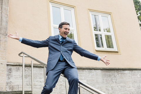 Carefree businessman sliding down railing in the city stock photo