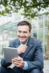 Porträt eines lächelnden Geschäftsmannes mit Tablet in der Stadt - MOEF01419