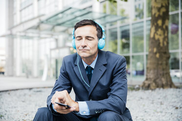 Businessman with closed eyes listening to music with headphones in the city - MOEF01423