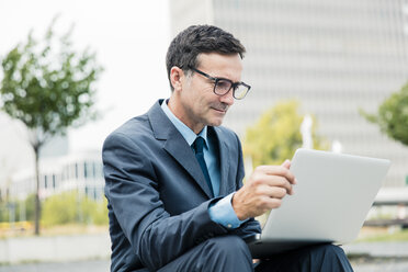 Businessman sitting down using laptop in the city - MOEF01434