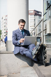 Businessman with inlineskates sitting down using laptop in the city - MOEF01439