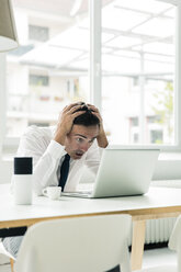 Geschockter Geschäftsmann schaut auf den Laptop auf dem Tisch im Büro - MOEF01449