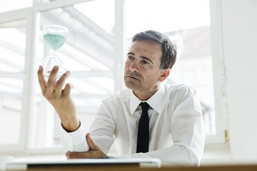 Serious businessman looking at hourglass in office - MOEF01455