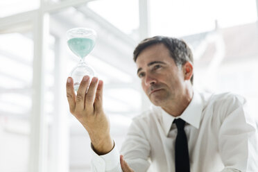 Seriöser Geschäftsmann mit Blick auf Sanduhr im Büro - MOEF01456