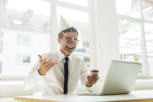 Lachender Geschäftsmann mit Laptop, der seinen Geburtstag im Büro feiert - MOEF01461