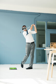 Businessman wearing VR glasses playing golf in office - MOEF01463