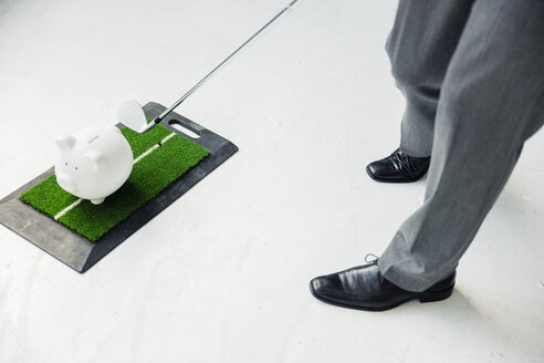 Close-up of businessman playing golf with piggy bank - MOEF01464